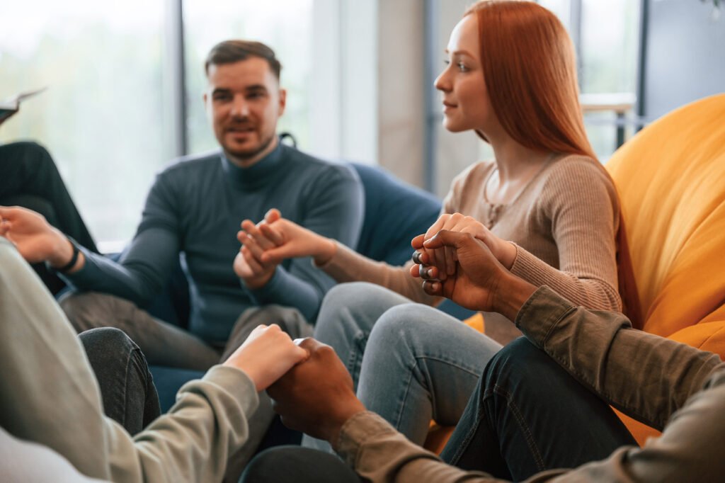 Sitting and holding each other by hands. Group of people are having therapy meeting together.